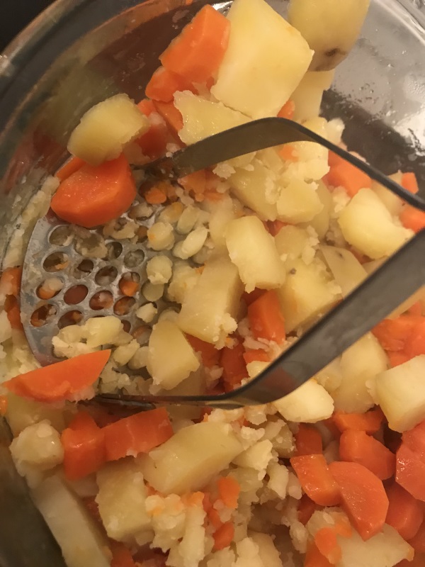 morceaux de carottes et de pommes de terre entrain d'être écrasé au presse-purée